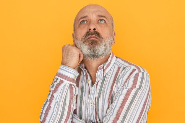 Portrait de séduisant homme âgé mal rasé avec tête chauve regardant avec des yeux pensifs pensifs, réfléchissant au problème, à la recherche d'une solution. Sentiments humains, réaction et langage corporel