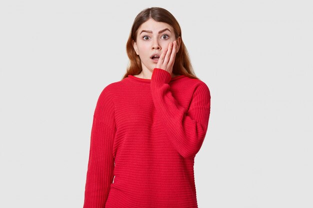 Portrait sensible de belle fille à la mode, vêtu d'un pull rouge posant sur blanc