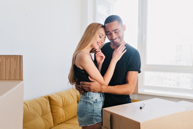 Portrait sensible de couple commençant une nouvelle vie ensemble, déménageant dans la maison, plat, se serrant dans les bras, touchant sensuellement dans l'appartement entre les boîtes