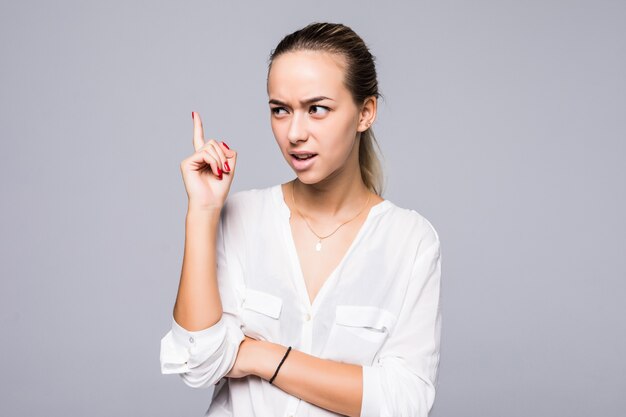 Portrait sérieux, fronçant les sourcils, en colère, grincheux jeune femme pointant le doigt vers le haut, gronder quelqu'un mur gris isolé