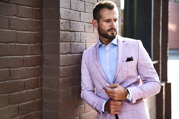 Portrait de sexy beau mannequin homme d'affaires habillé en costume élégant posant près du mur de briques sur le fond de la rue. Métrosexuel