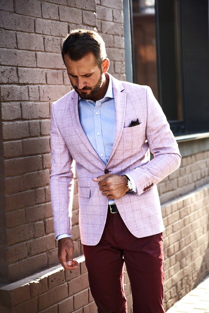 Portrait de sexy beau mannequin homme d'affaires habillé en costume élégant posant près du mur de briques sur le fond de la rue. Métrosexuel