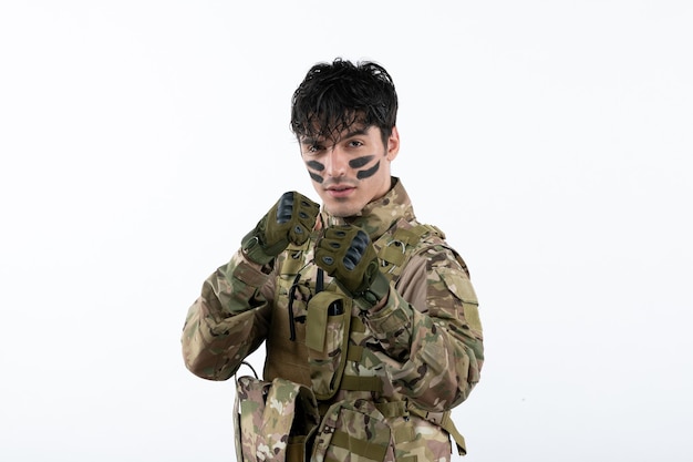 Portrait d'un soldat masculin en tenue de camouflage prêt à se battre sur un mur blanc