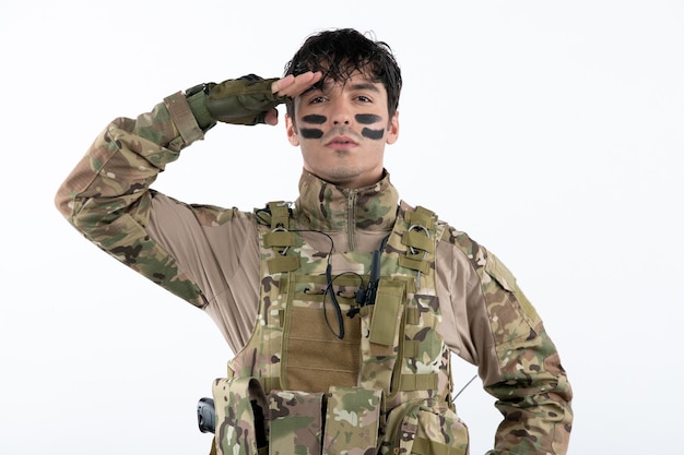 Portrait d'un soldat masculin en tenue de camouflage saluant sur un mur blanc