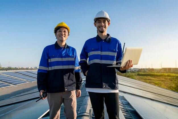 Portrait souriant ingénieur professionnel avec ordinateur portable et tablette vérification de l'entretien de l'installation du panneau de toit solaire sur le toit de l'usine sous la lumière du soleil Enquête de l'équipe d'ingénieurs vérifier le toit du panneau solaire