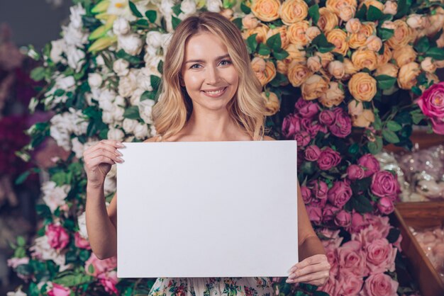 Portrait souriant d&#39;une jeune femme blonde montrant une carte blanche vierge