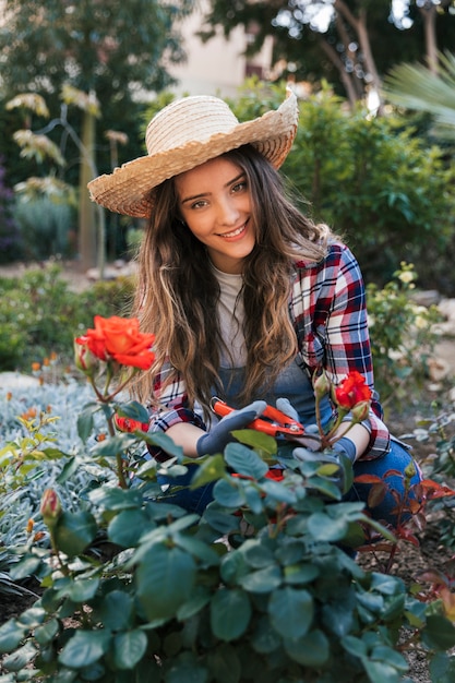 Photo gratuite portrait souriant d'une jeune femme coupant la belle rose adulte avec des cisailles