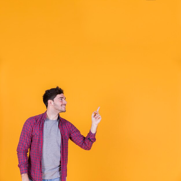 Portrait souriant d&#39;un jeune homme montrant quelque chose sur un fond orange