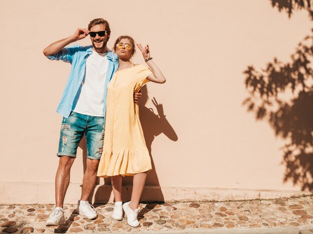 Portrait de souriante belle fille et son beau petit ami. Femme en robe d'été décontractée et homme en jeans. Famille joyeuse heureuse. Femme s'amusant dans la rue près du mur