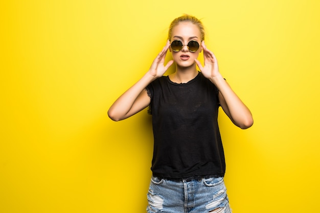 Portrait de sourire belle fille blonde à lunettes de soleil sur fond jaune