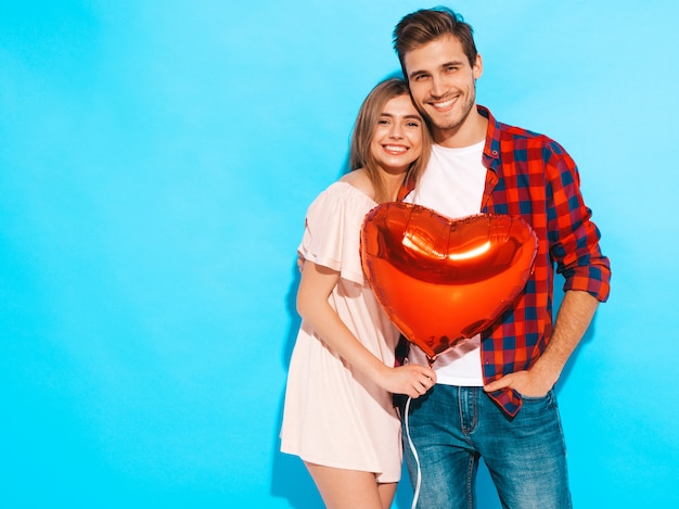 Portrait de sourire belle fille et son beau petit ami tenant des ballons en forme de coeur et rire. Couple heureux en amour. Joyeuse saint Valentin