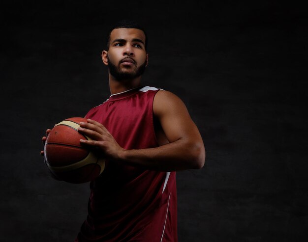 Portrait d'un sportif afro-américain. Joueur de basket-ball en tenue de sport avec un ballon sur fond sombre.