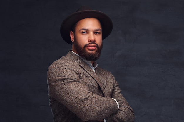 Photo gratuite portrait en studio d'un beau mâle afro-américain dans une élégante veste marron et un chapeau. isolé sur un fond sombre.