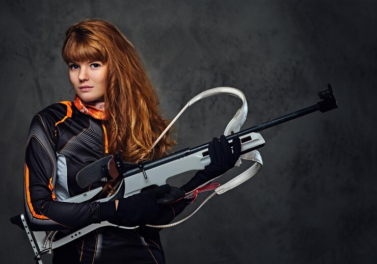 Photo gratuit portrait en studio d'une championne de biathlon à tête rouge tenant une arme à feu sur fond gris.