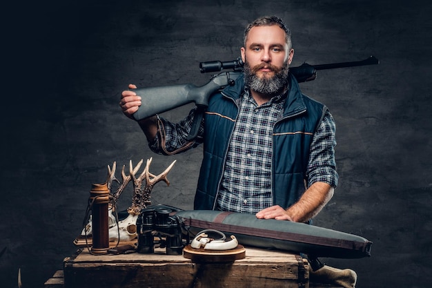 Portrait en studio d'un chasseur moderne barbu avec son trophée tenant un fusil.