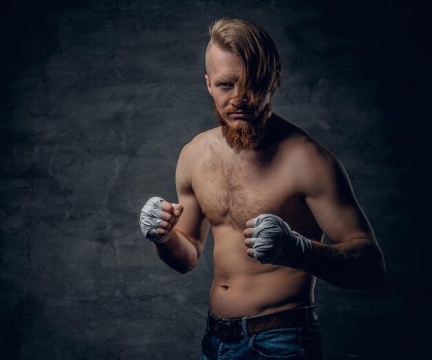 Portrait en studio d'un combattant brutal à tête rousse barbu aux cheveux longs sur fond gris foncé.