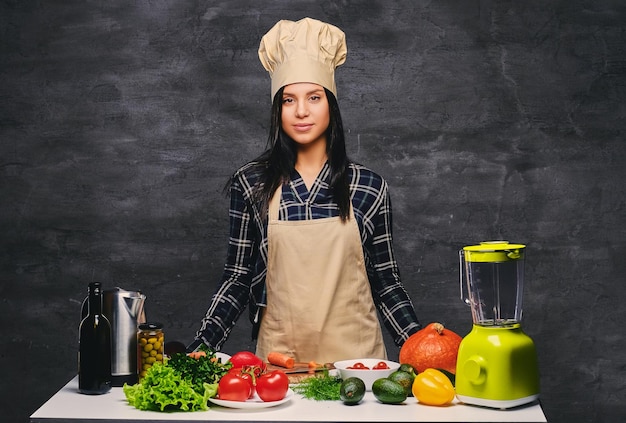 Portrait en studio du chef cuisinier féminin à la table avec beaucoup de légumes.