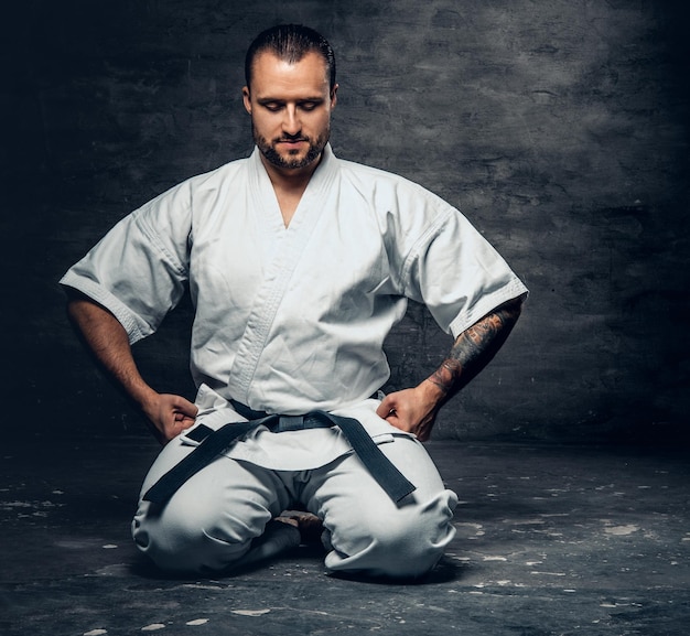 Photo gratuite portrait en studio du combattant de karaté brutal barbu vêtu d'un kimono blanc sur fond gris.