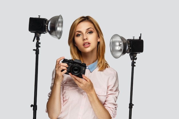 Portrait en studio d'une femme blonde positive avec appareil photo avec équipement photo sur fond.