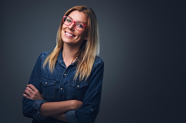 Portrait en studio d'une femme blonde vêtue d'une chemise en jean et de lunettes rouges.