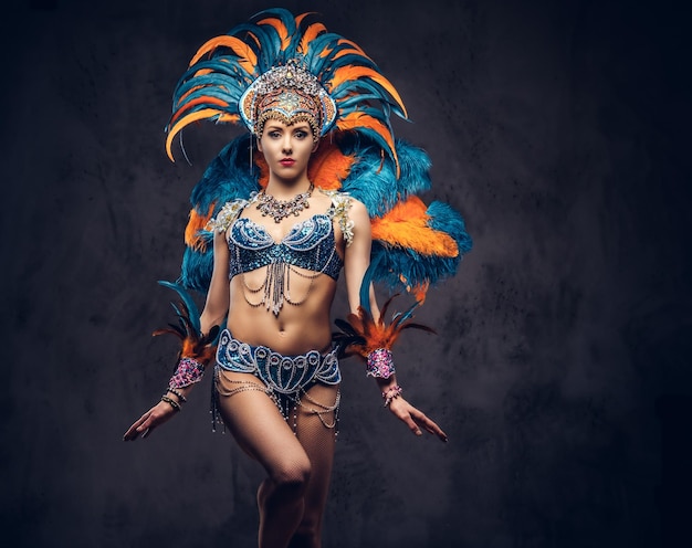 Portrait en studio d'une femme sexy dans un somptueux costume de plumes de carnaval coloré, posant sur un fond sombre.