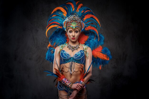 Portrait en studio d'une femme sexy dans un somptueux costume de plumes de carnaval coloré, posant sur un fond sombre.