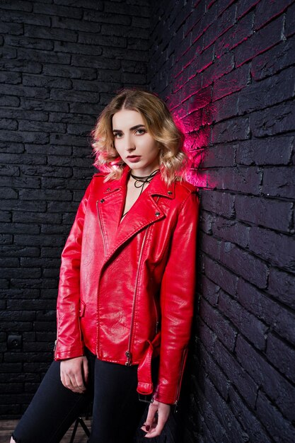 Portrait en studio de fille blonde en veste de cuir rouge contre le mur de briques