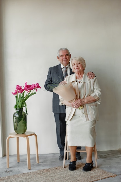 Portrait en studio de l'heureux couple de personnes âgées embrassant contre le mur gris.