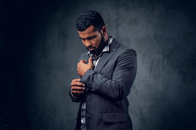 Portrait en studio d'un hipster noir vêtu d'une chemise polaire et d'une veste posant sur un fond artistique gris.