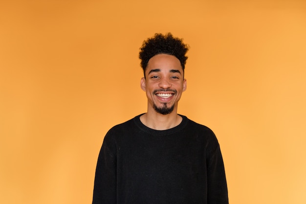 Photo gratuite portrait en studio d'un homme afro-américain portant un pull noir souriant sur un mur orange.