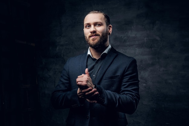 Portrait en studio d'un homme barbu aux bras croisés, vêtu d'une veste bleue sur fond de vignette grise.