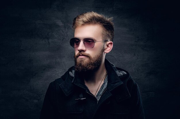 Portrait en studio d'un homme barbu à la mode en lunettes de soleil sur fond de vignette grise.