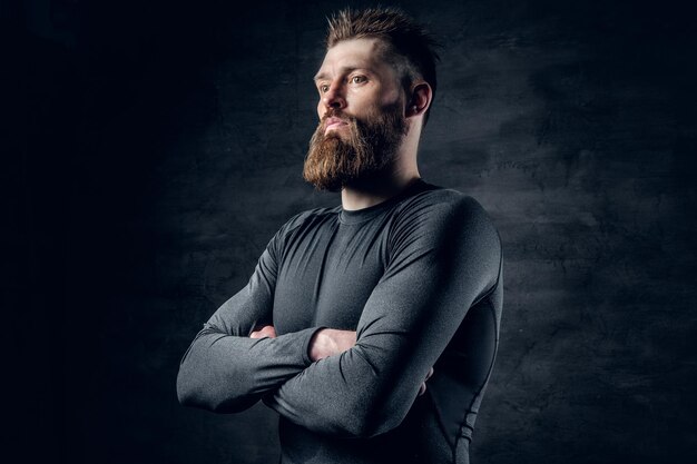 Portrait en studio d'un homme barbu sportif vêtu d'un vêtement de sport gris sur fond gris foncé.