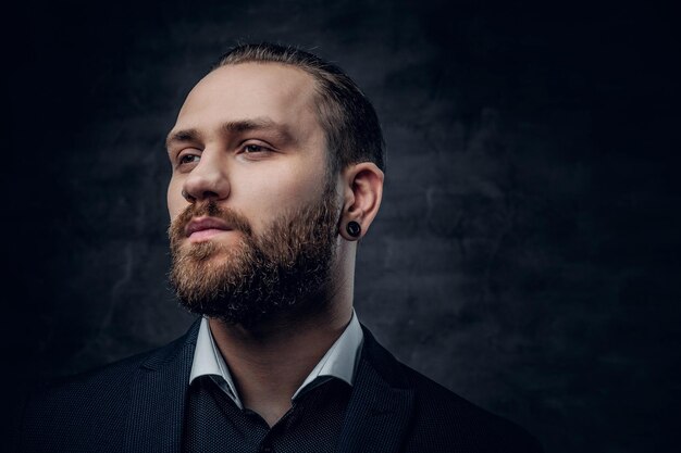 Portrait en studio d'un homme barbu vêtu d'une veste bleue sur fond de vignette grise.