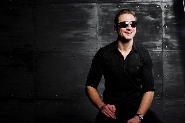 Portrait en studio d'un homme élégant portant une chemise noire et des lunettes contre un mur en acier