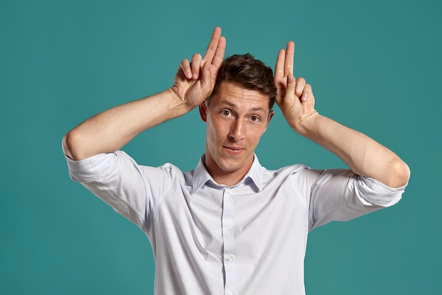 Portrait en studio d'un jeune brun dans une chemise blanche classique agissant comme s'il était une vache tout en posant sur un fond bleu. Coupe de cheveux élégante. Concept d'émotions sincères. Copiez l'espace.