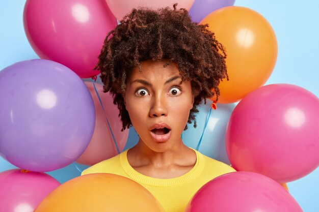 Portrait en studio d'une jeune femme étonnée posant entourée de ballons colorés d'anniversaire