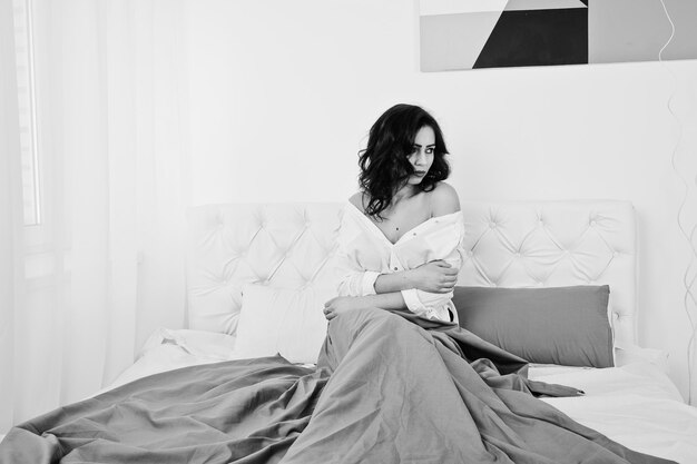 Portrait en studio de jeune fille brune en blouse blanche allongée sur le lit