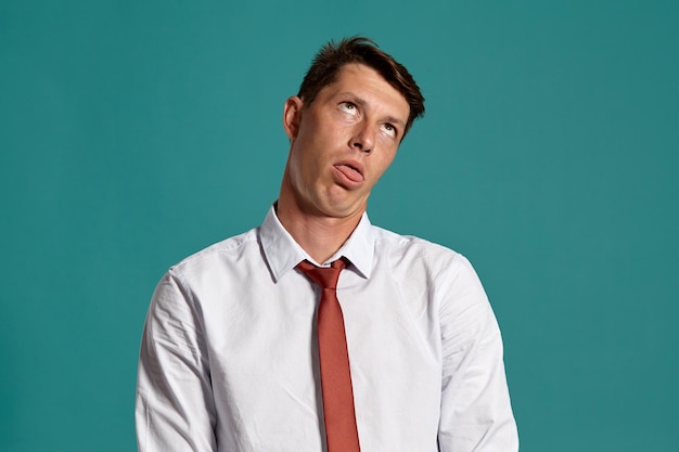 Portrait en studio d'un jeune homme d'affaires charismatique dans une chemise blanche classique et une cravate rouge à la colère tout en posant sur un fond bleu. Coupe de cheveux élégante. Concept d'émotions sincères. Copiez l'espace.