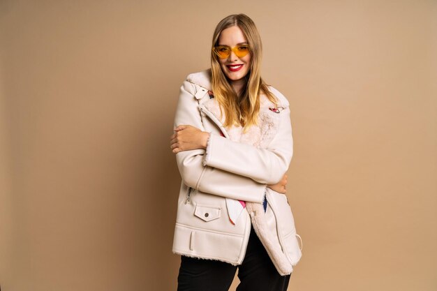 Portrait en studio à la mode d'une belle femme blonde portant une veste à la mode en fourrure et une écharpe colorée fond beige automne hiver saison d'automne