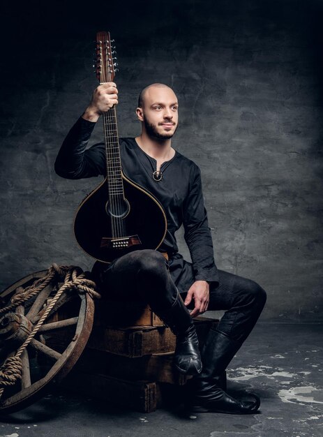 Le portrait en studio d'un musicien folklorique traditionnel vêtu de vêtements celtiques vintage est assis sur une boîte en bois et tient une mandoline.