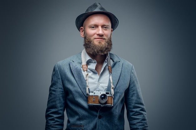 Portrait en studio d'un photographe barbu vêtu d'un costume et d'un chapeau en feutre contenant un vieil appareil photo SLR vintage.