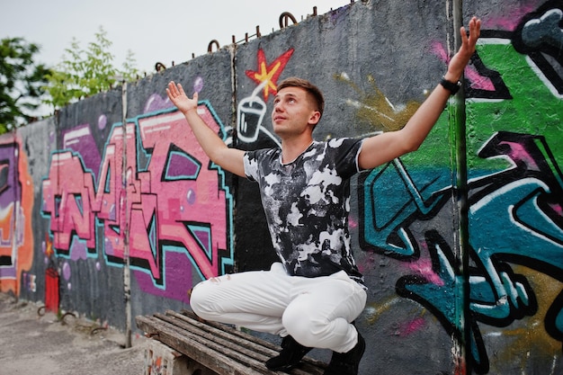 Portrait de style de vie d'un bel homme posant dans la rue de la ville avec un mur de graffitis