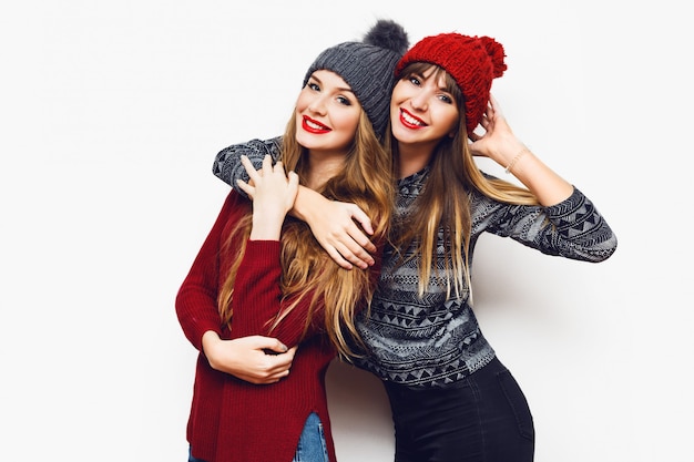 Portrait de style de vie intérieur de deux femmes assez heureuses, meilleurs amis dans de jolis chapeaux tricotés et des chandails confortables s'amusant