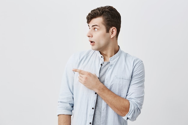 Portrait à la taille d'un homme de race blanche confus avec des yeux sur écoute gesticulant avec un regard choqué à l'espace de copie de fond gris montrant la place pour votre texte ou des informations promotionnelles. Publicité masculine