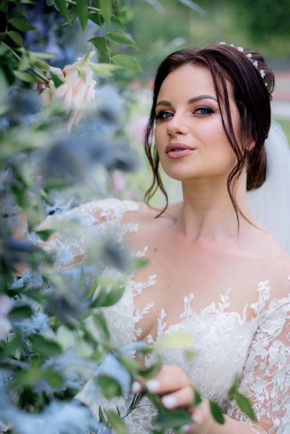 Portrait tendre de la belle mariée brune près de feuilles vertes, jour du mariage