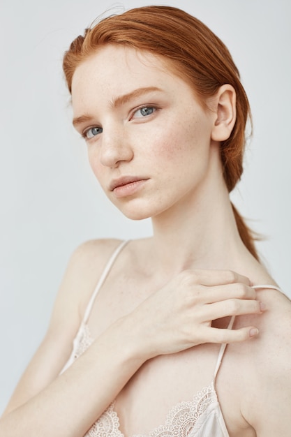 Portrait de tendre belle rousse sur mur blanc.