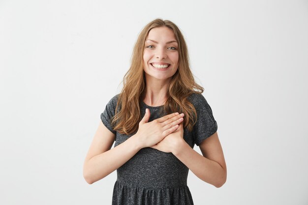 Portrait de tendre heureuse jeune fille souriante tenant par la main sur le coeur.