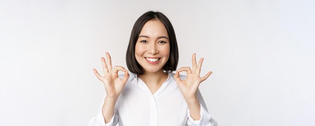 Portrait de tête en gros plan d'une fille asiatique montrant un signe correct ok et souriant satisfait recommandant d'être heureux de louer et de faire un compliment sur fond blanc