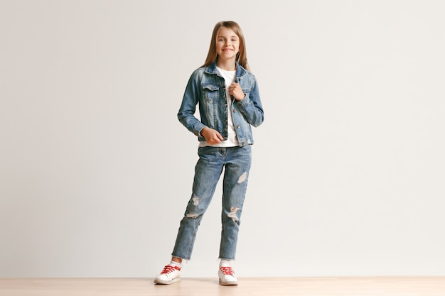 Portrait de toute la longueur de la jolie petite adolescente dans des vêtements de jeans élégants souriant